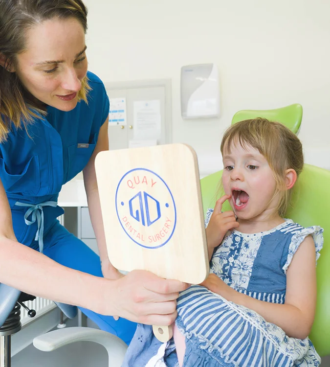 Dental nurse holding a Quay Dental card for a young girl in the dental chair
