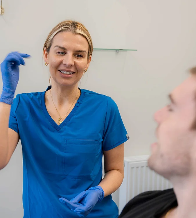 Smiling dentist in blue scrubs giving advice to a patient