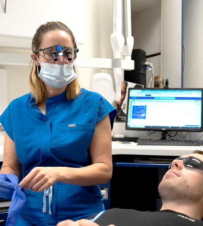 Dentist wearing magnifying loupes reassuring a reclined patient