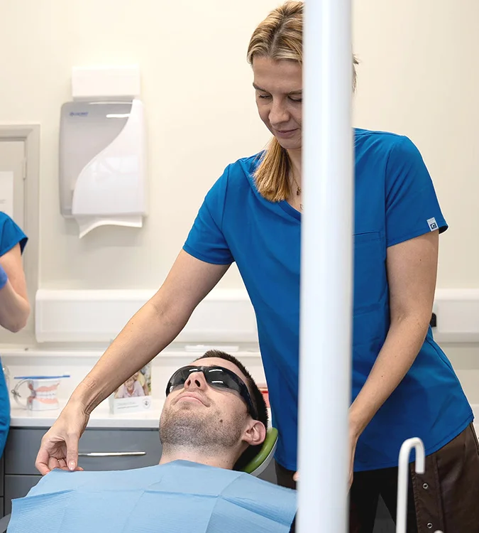 Dental clinician standing beside a patient wearing protective glasses