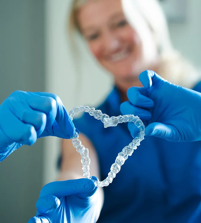 Gloved hands holding a clear Invisalign aligner